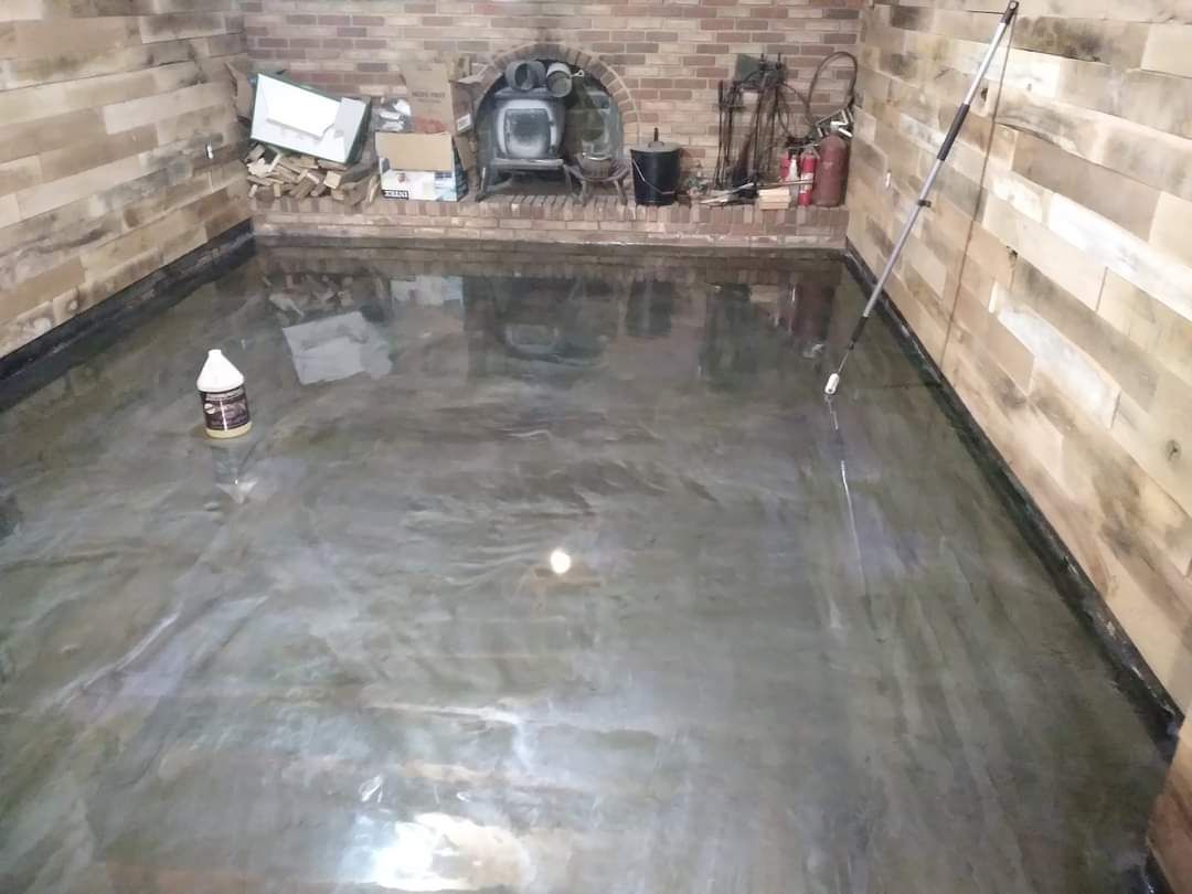 A room with wood-paneled walls, a fireplace, and a freshly applied, reflective gray metallic epoxy floor.