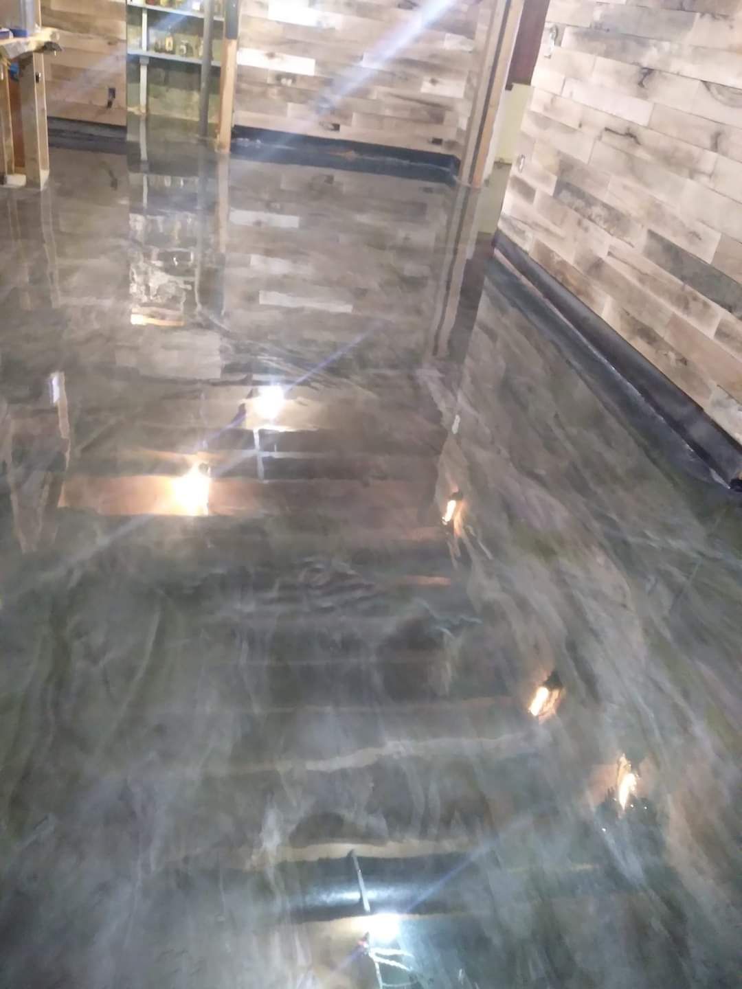 High-gloss grey epoxy floor with a swirling, marbled finish, next to a wood-paneled wall.
