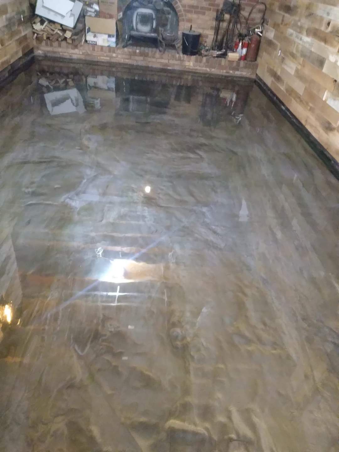A room with a polished, high-gloss, brown-toned epoxy floor with marbled patterns, facing a brick fireplace.