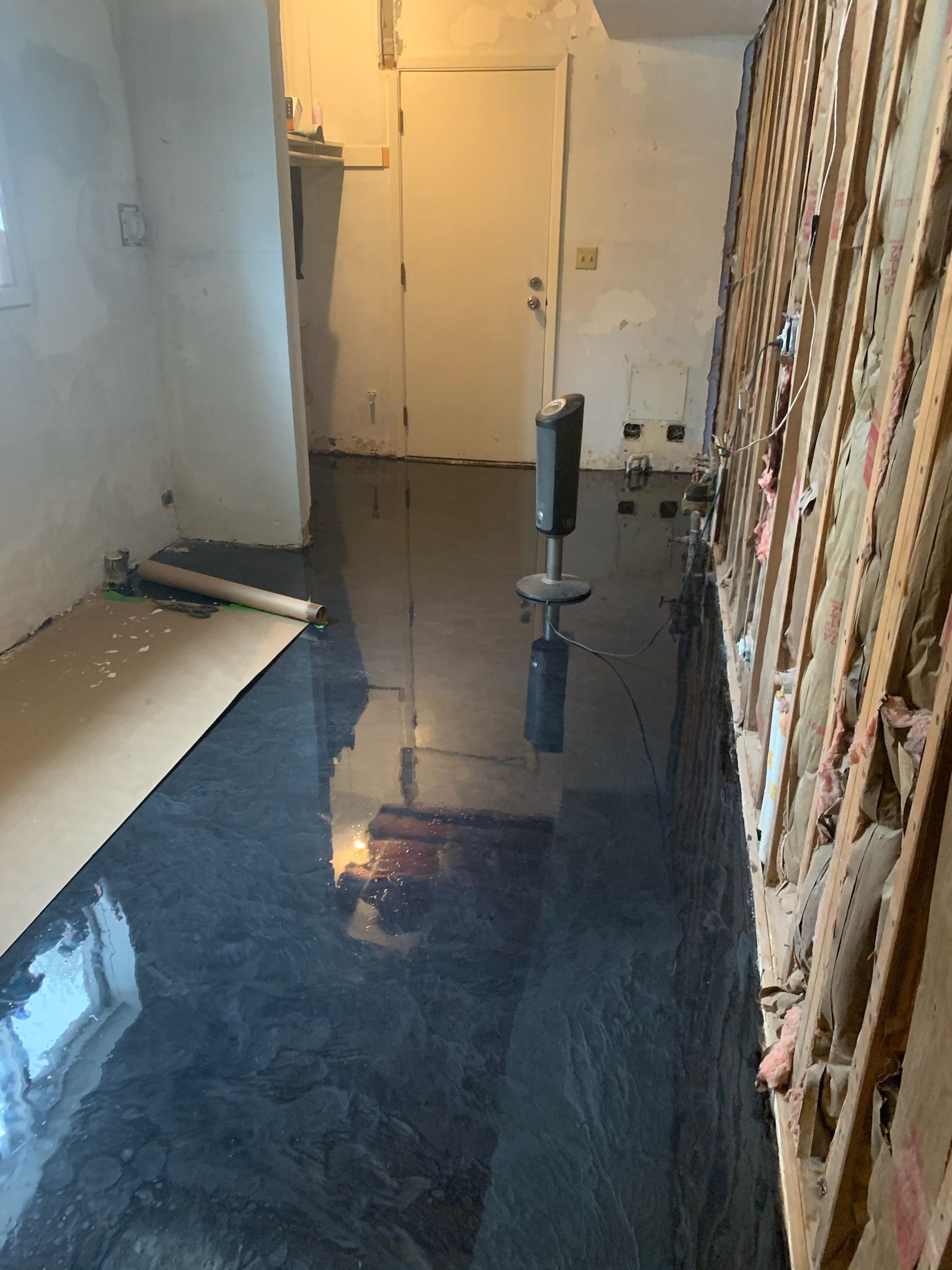 A room under renovation with a high-gloss, dark grey metallic epoxy floor, an upright heater, and exposed wall studs.