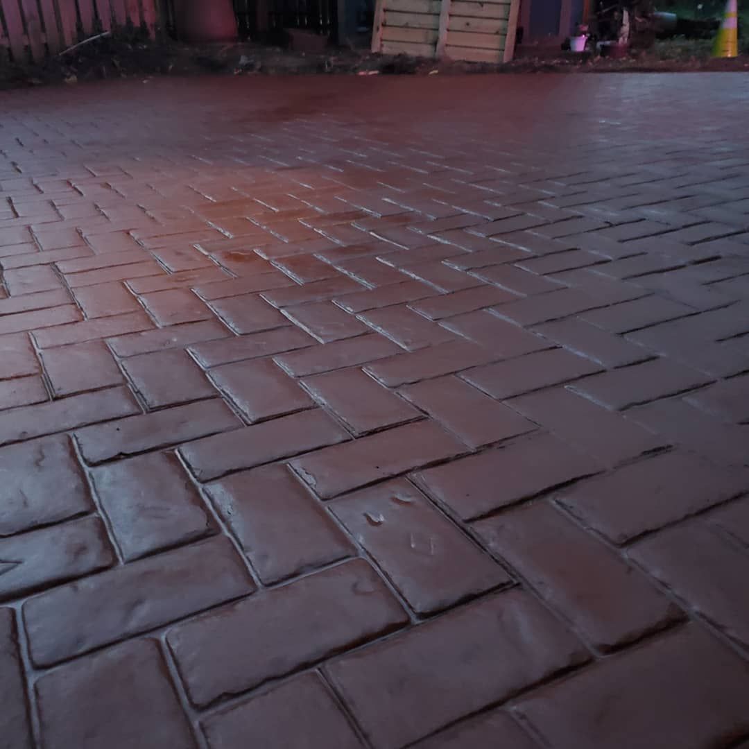 A reddish-brown concrete surface with a stamped herringbone brick pattern.