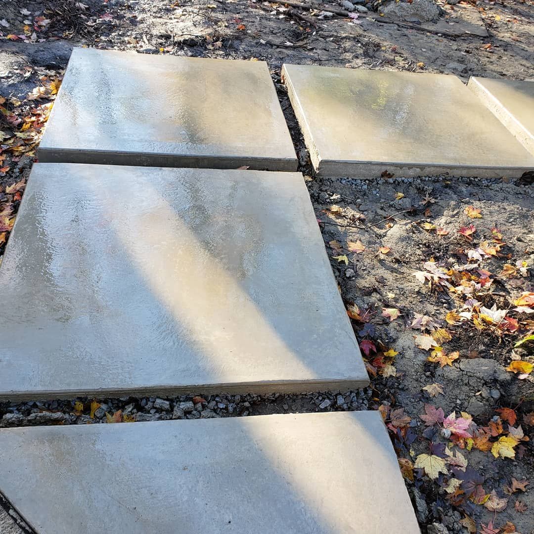 Four large concrete square pavers are set in the ground, partially surrounded by dirt and fallen autumn leaves.