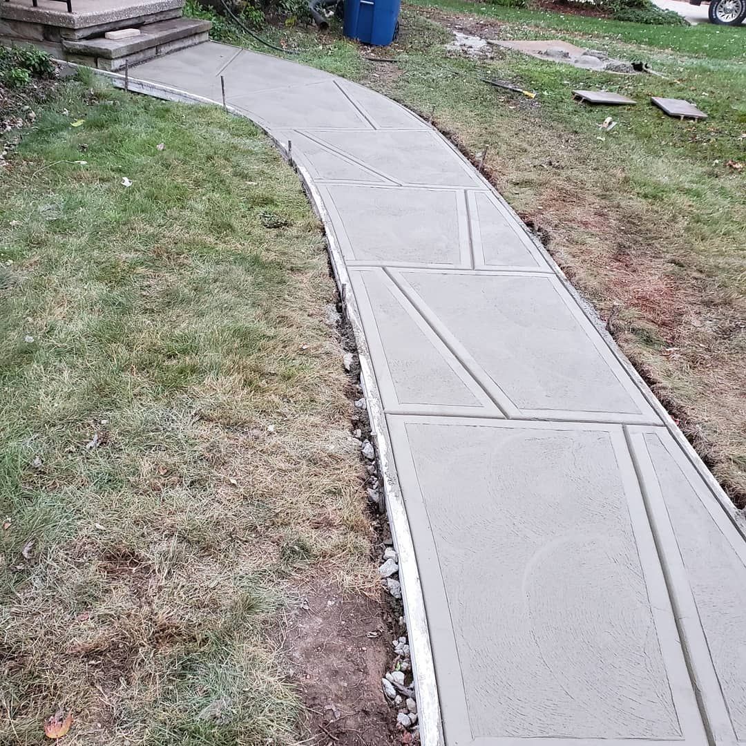 A curved, freshly poured concrete walkway leading to front steps, with construction form boards along the edges.