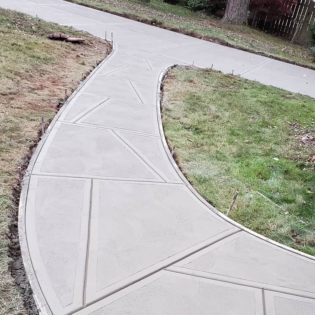 A curved concrete walkway outdoors with decorative geometric score lines, bordered by grass.