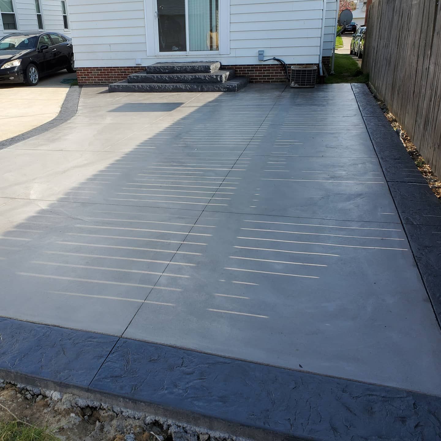 A freshly poured gray concrete driveway with a dark textured stamped border leading to a house entrance.