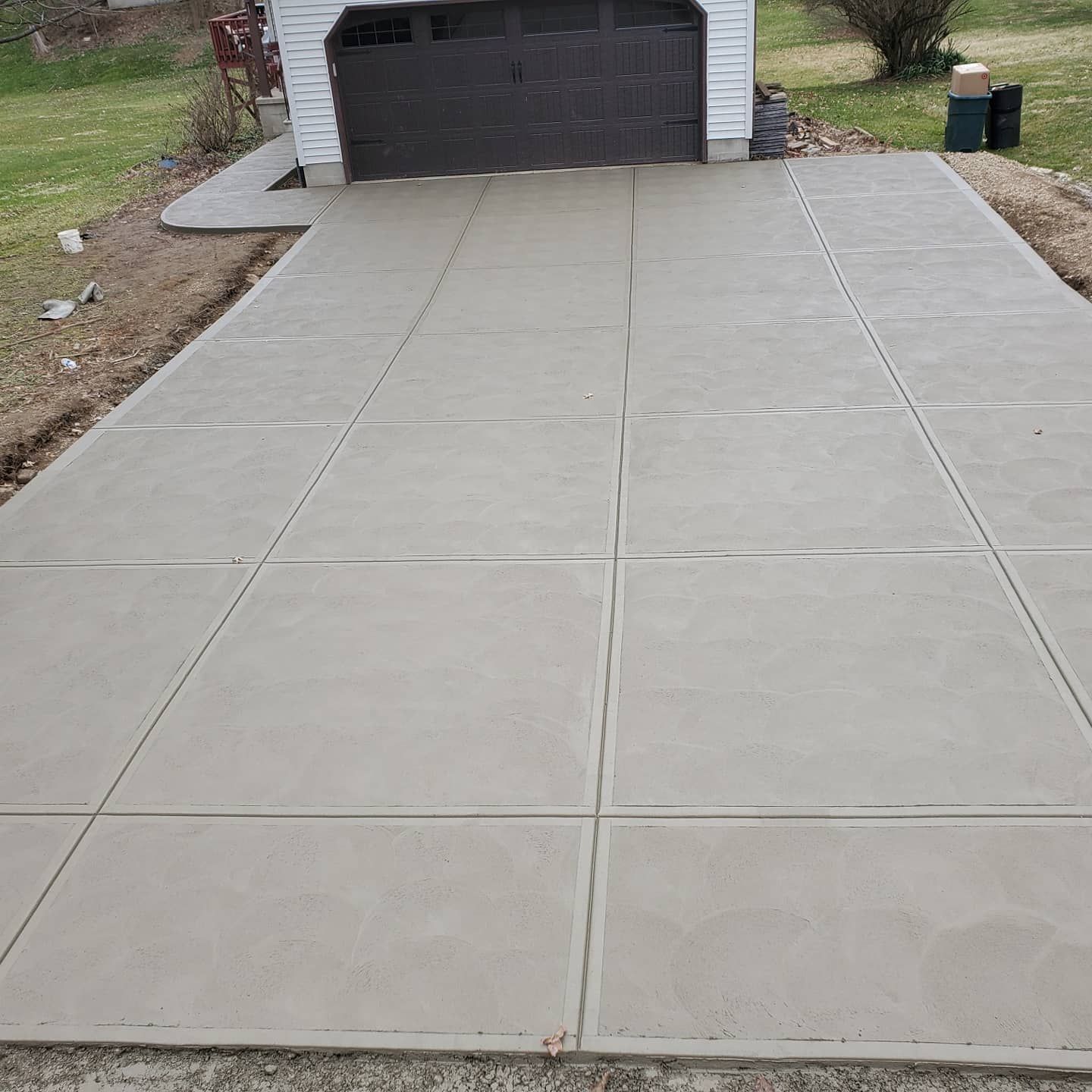 A newly poured concrete driveway with a grid of control joints leading to a garage door.