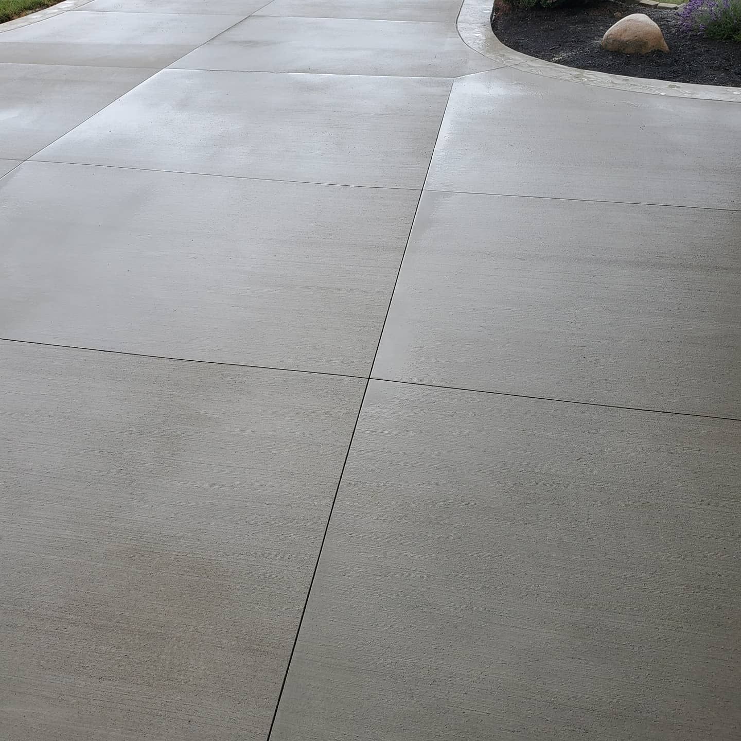 A gray concrete driveway featuring rectangular paving sections separated by dark, straight control joints.