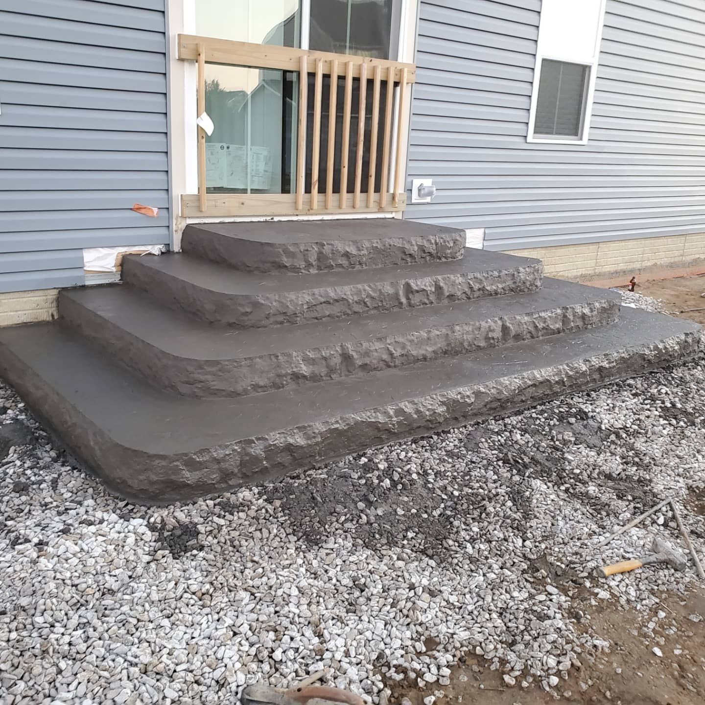 Newly installed dark gray concrete steps leading to a sliding glass door on a house with gray vinyl siding.