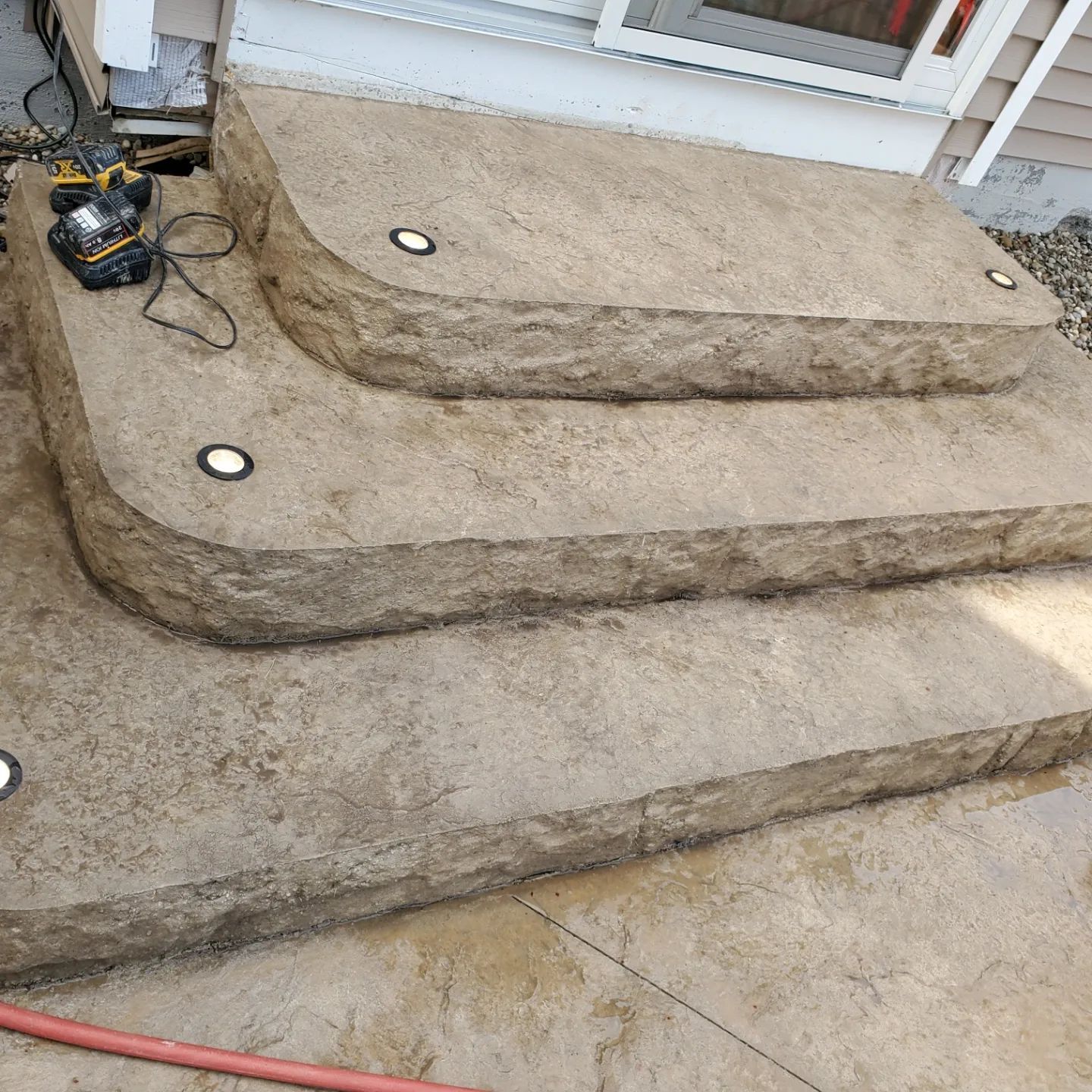 Three tiered stone steps leading to a house door with integrated circular recessed lights in the treads.