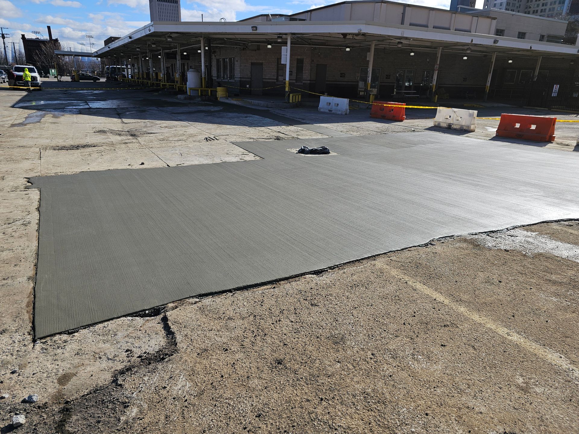 A freshly poured concrete patch in a weathered outdoor parking lot, near a building with a covered loading dock.