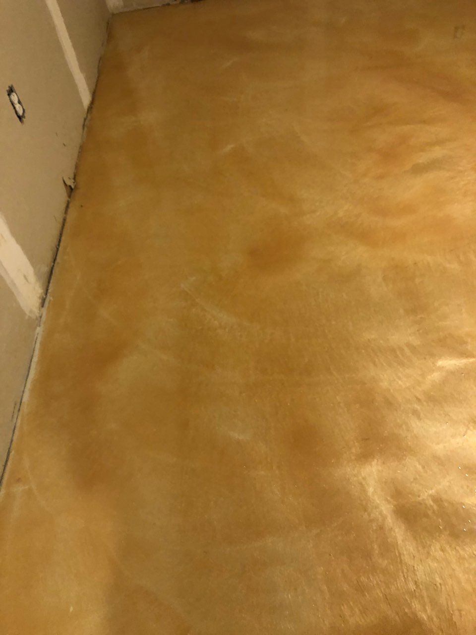 A high-angle view of a floor covered in freshly applied, amber-colored concrete stain with a mottled, textured finish.