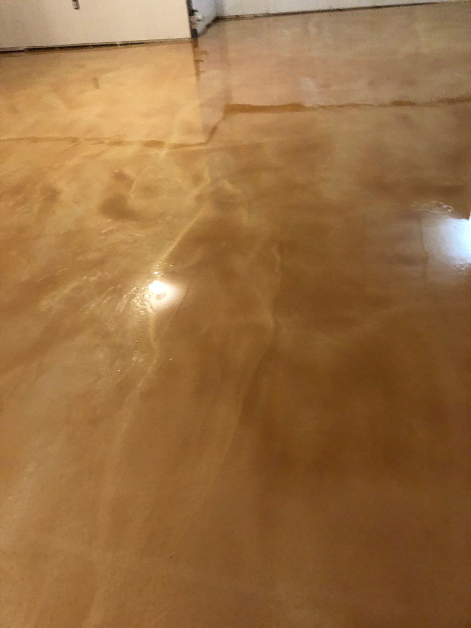 A close-up of a glossy, light brown metallic epoxy floor with a smooth, marbled finish.