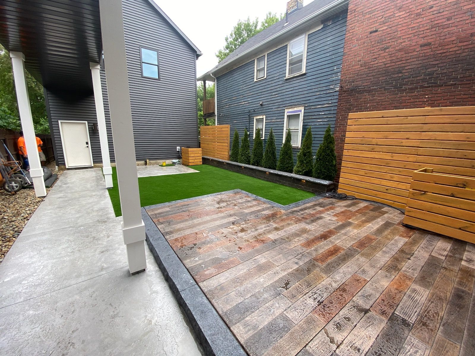 A modern residential backyard featuring a paver patio, small artificial turf lawn, and horizontal wood privacy fencing.