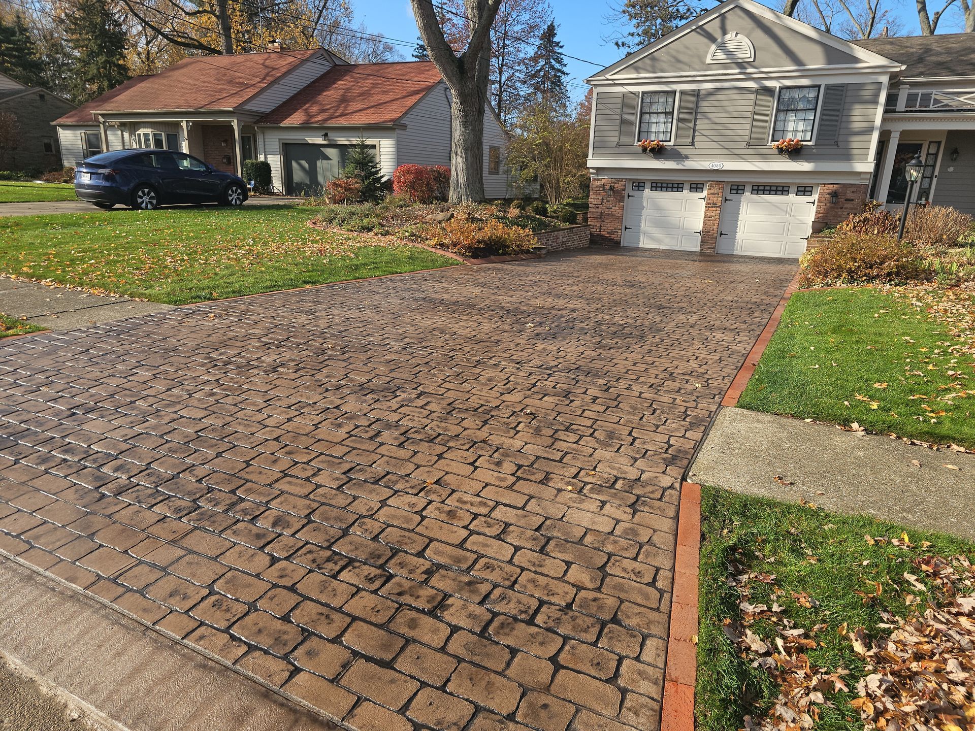 A multi-toned, cobblestone driveway leads to a two-car garage of a suburban house on a sunny, autumn day.