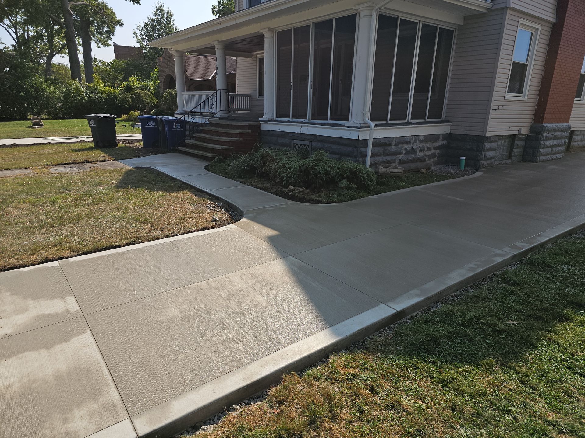 A newly poured concrete driveway and walkway leading to the front porch of a house with light-colored siding.