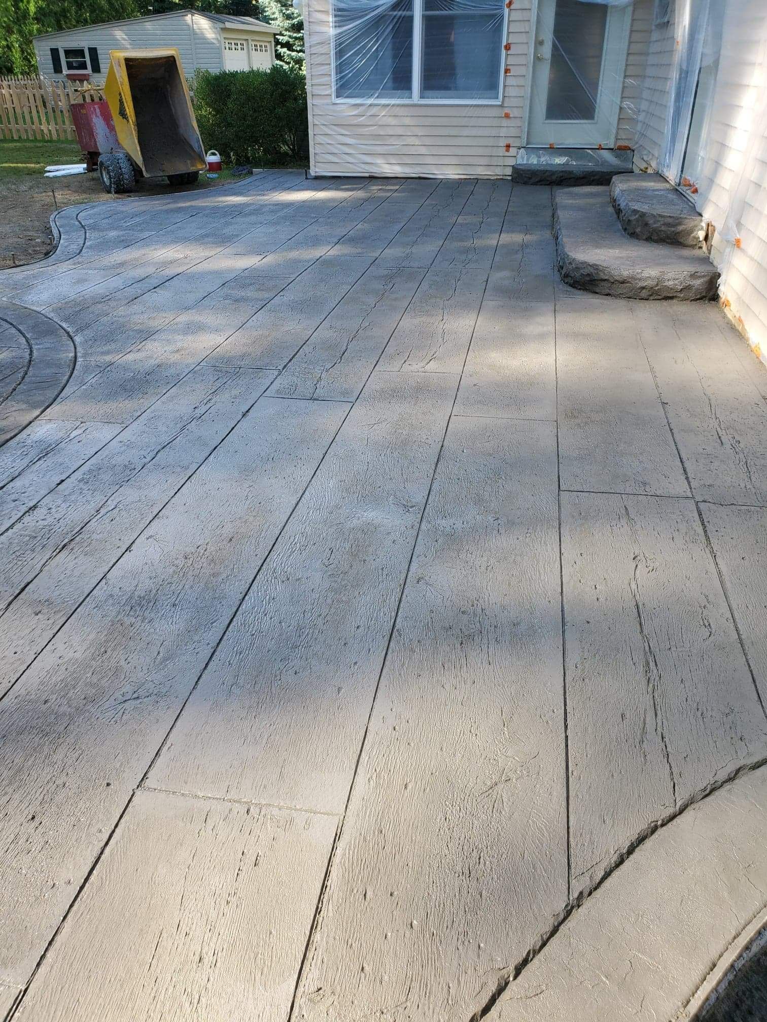 A newly poured stamped concrete patio outside a house with a yellow dumpster in the background.
