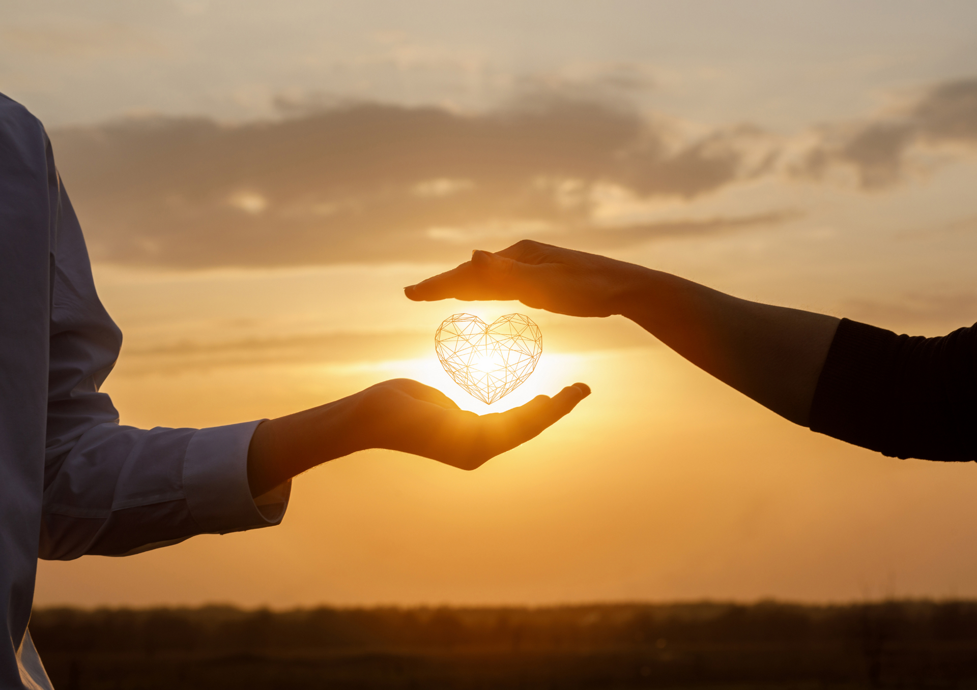 Two hands cupping a glowing heart, set against an orange sunset.