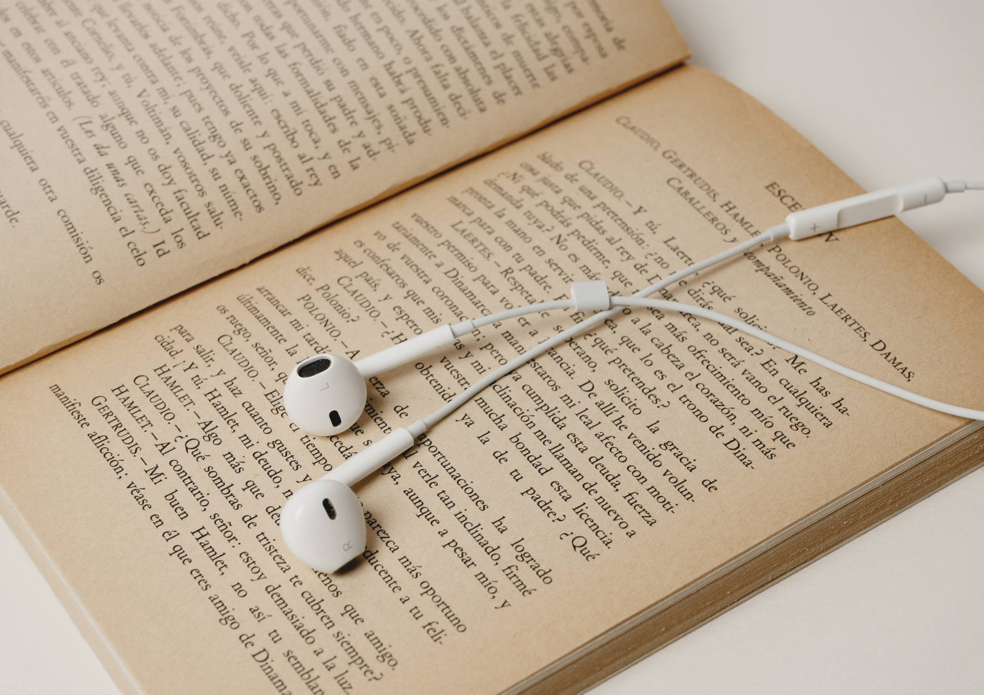 White earbuds resting on an open book, pages with printed text.