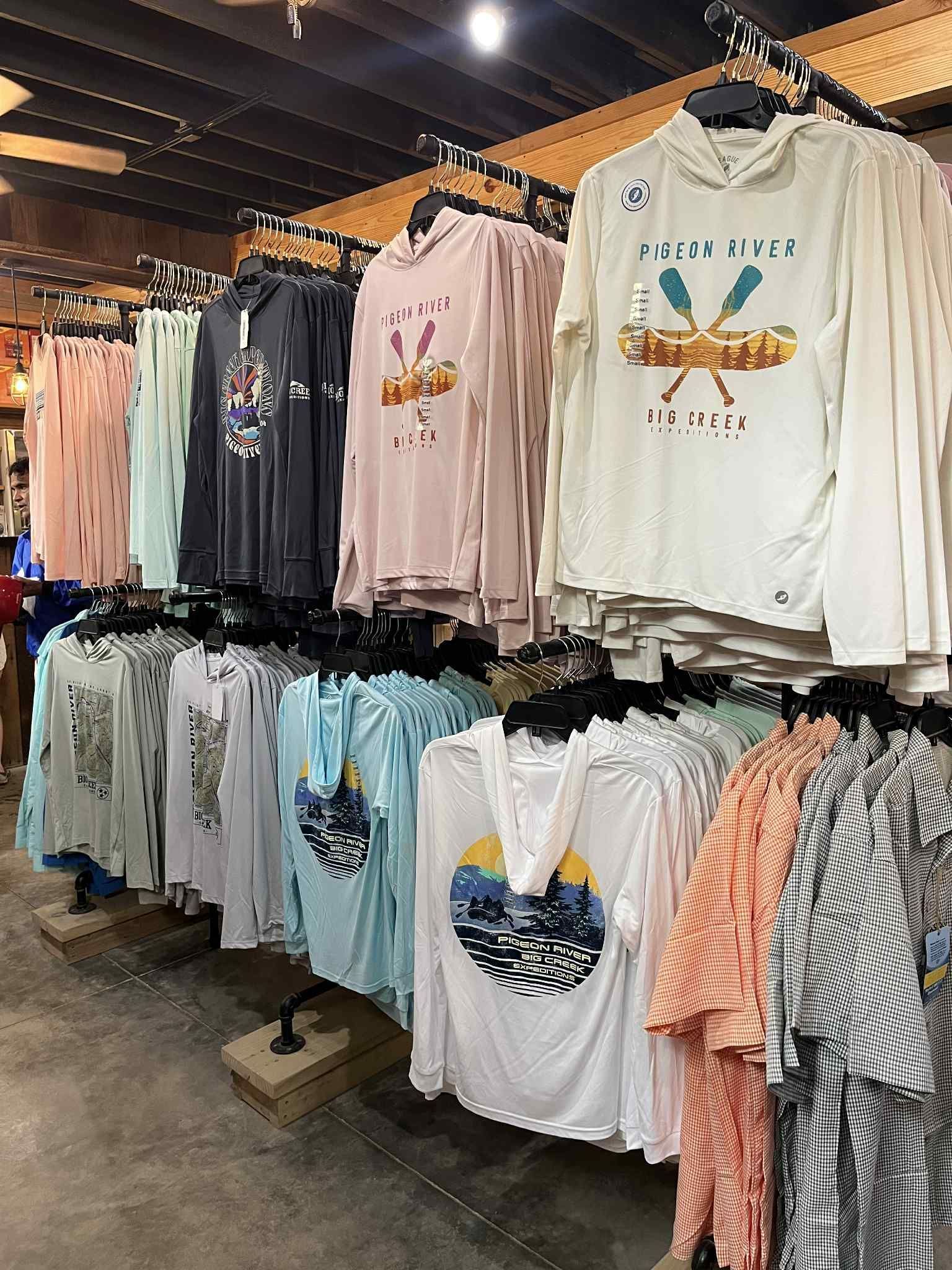 A clothing store display featuring various long-sleeved hooded shirts with outdoor-themed graphic prints on hangers.