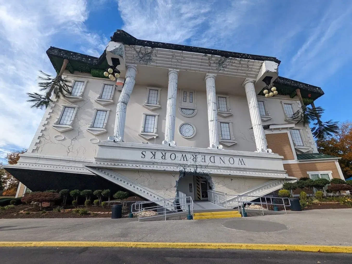 White upside-down building facade with columns and a sign, viewed from below against a blue sky