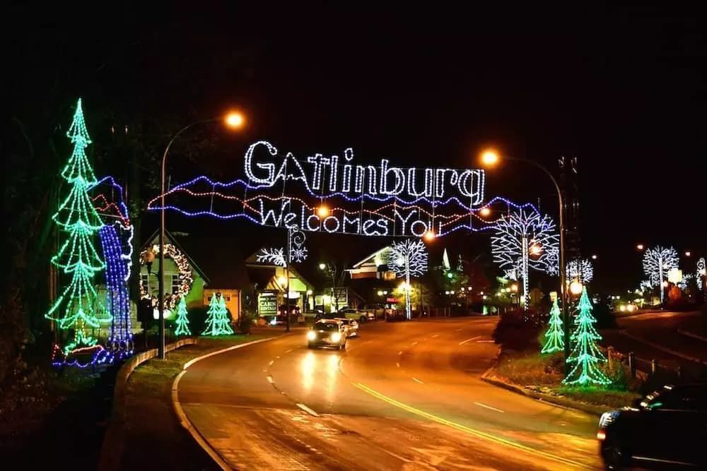 Gatlinburg welcomes visitors with a festive, illuminated archway and Christmas lights along a road at night.