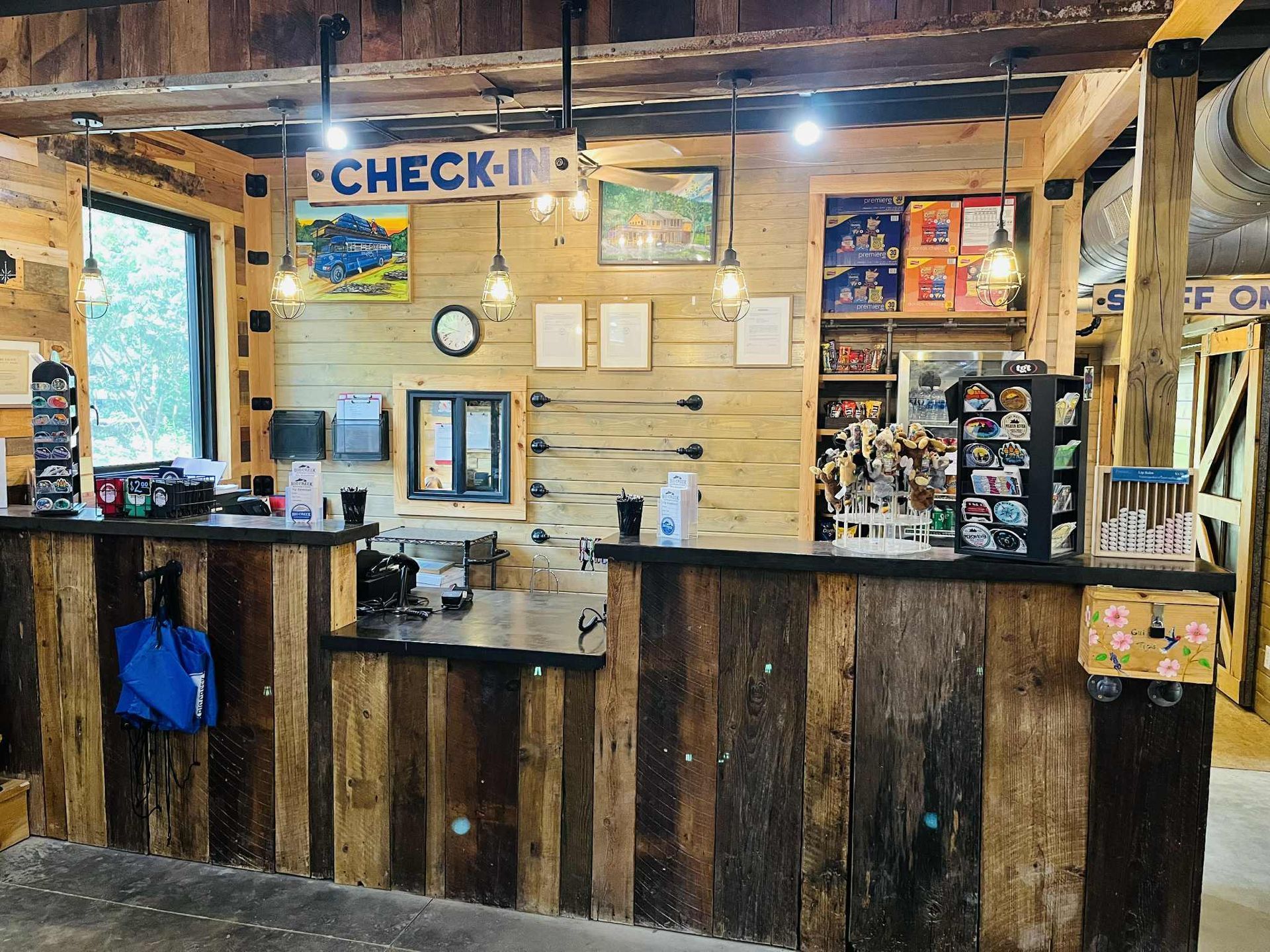 A rustic-style check-in counter made of wood planks in a cabin-like interior, featuring a sign and merchandise shelving.