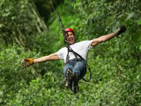 Person zip-lining through a green forest, arms outstretched and smiling in a red helmet
