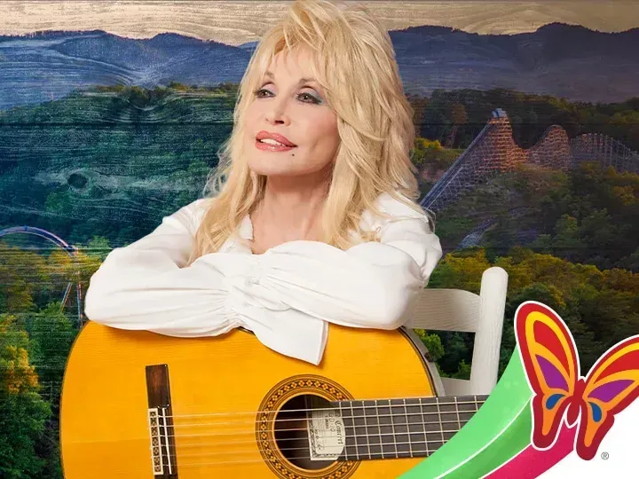 Blonde woman in a white blouse leaning on a yellow guitar against a scenic mountain backdrop