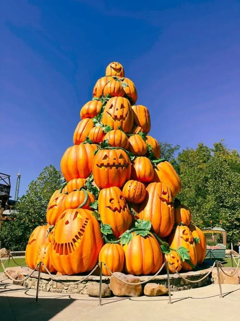 A pyramid of carved orange pumpkins stacked outdoors under a blue sky