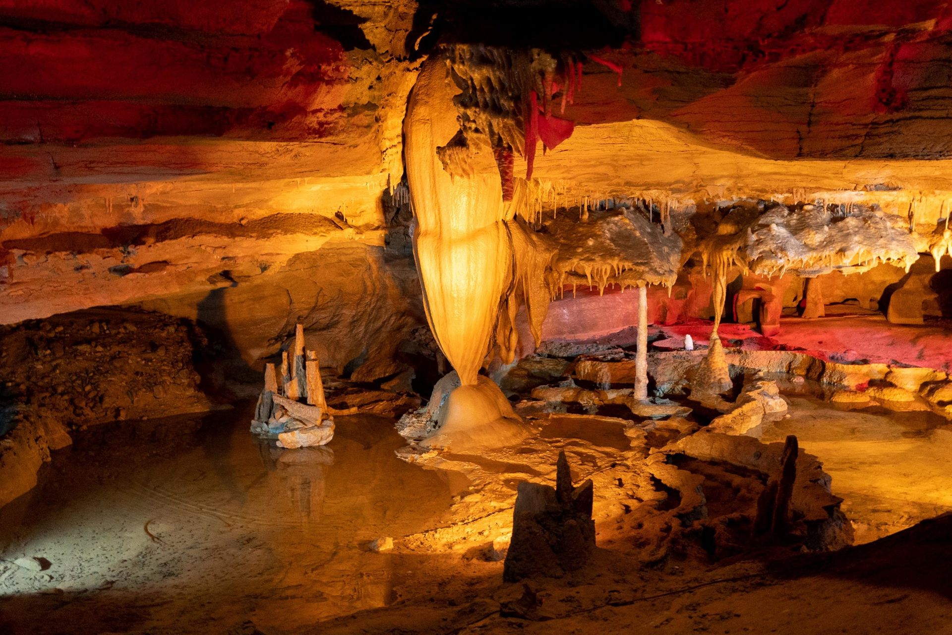 Colorful illuminated cave with stalactites, rock formations, and a small boat on an underground lake