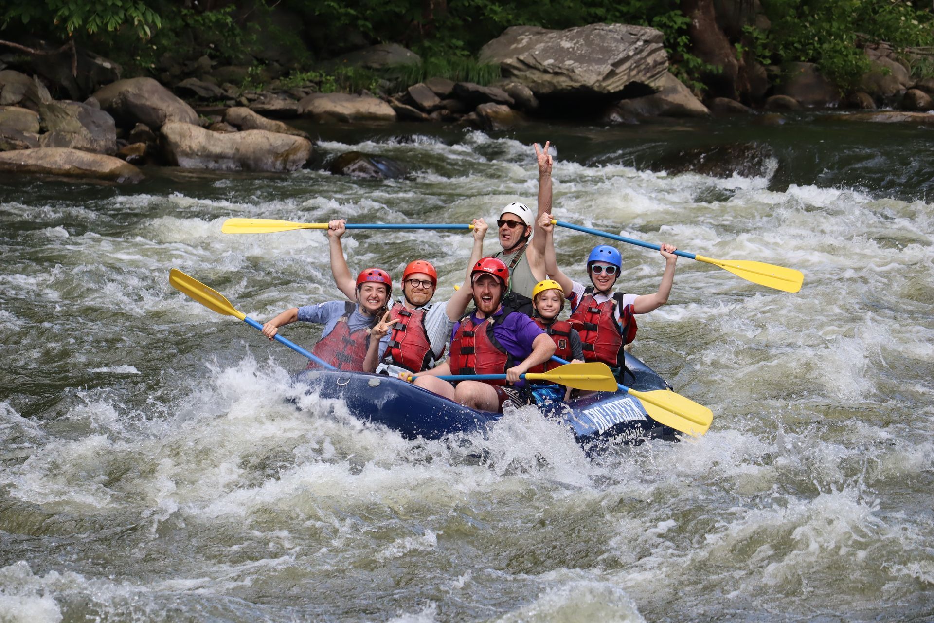 White-water rafters in red life jackets paddling a blue raft through rushing rapids