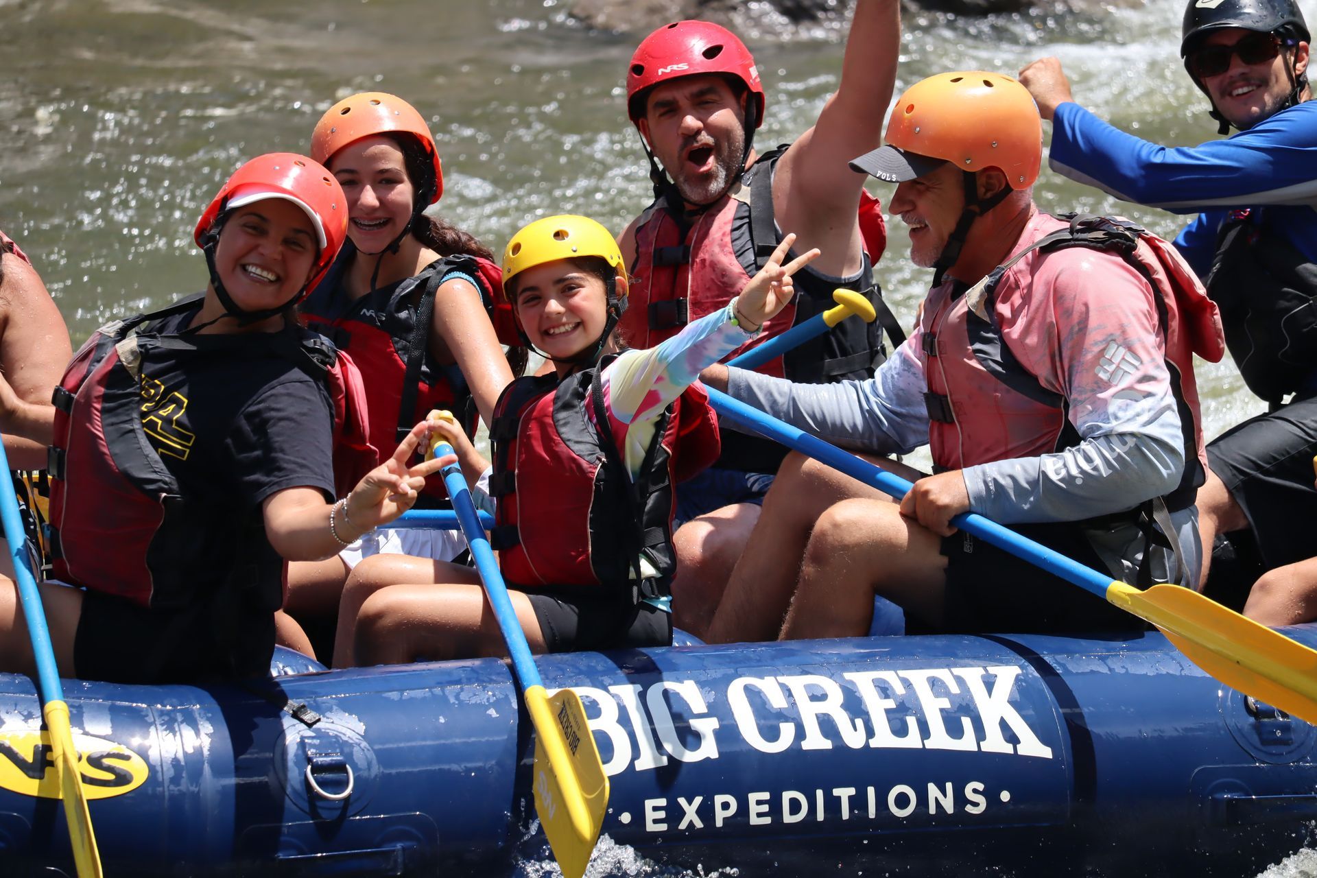 Rafting group in helmets and life vests cheering on a blue Big Creek Expeditions raft