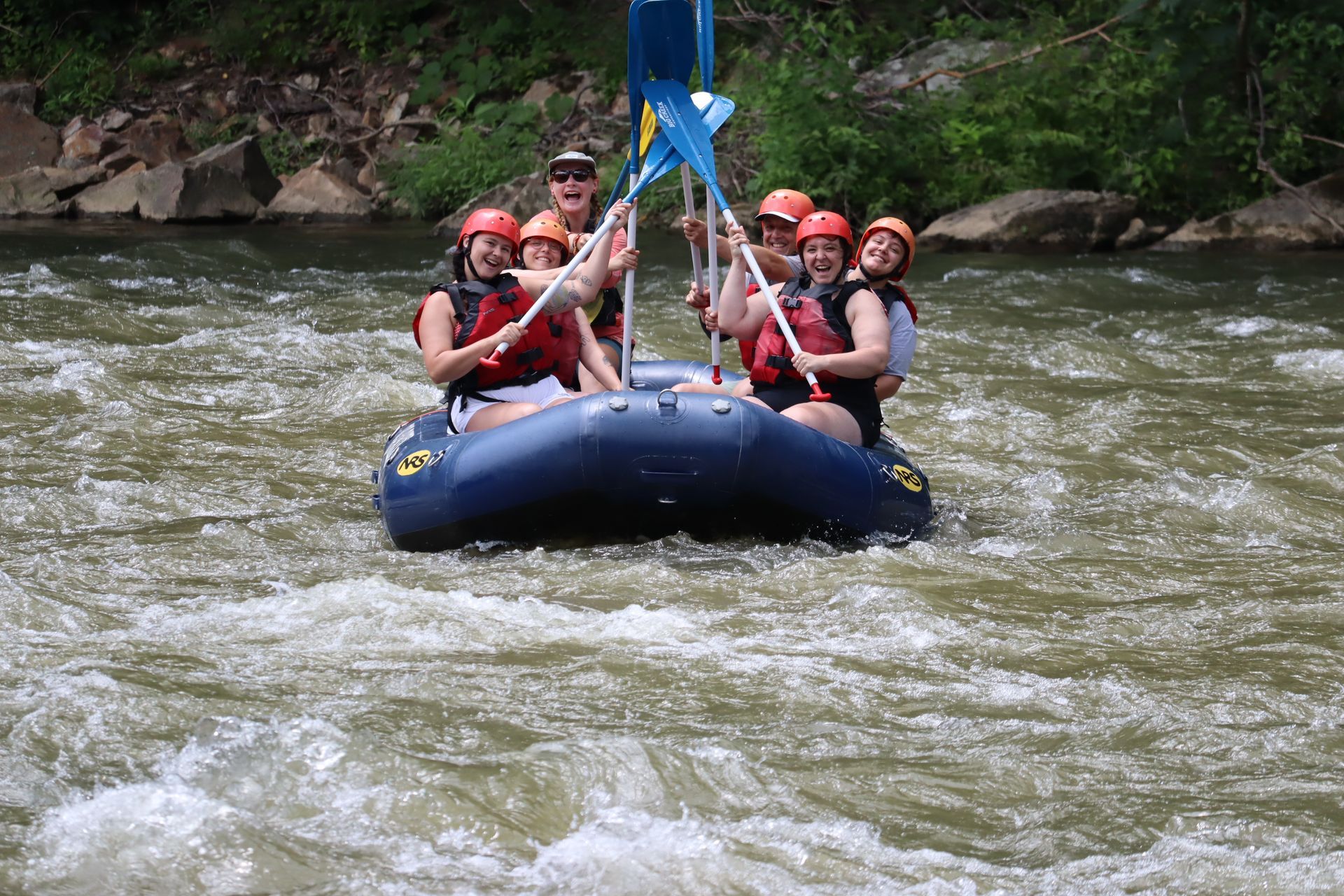 Rafting group in helmets paddles through rough river rapids under a blue support line