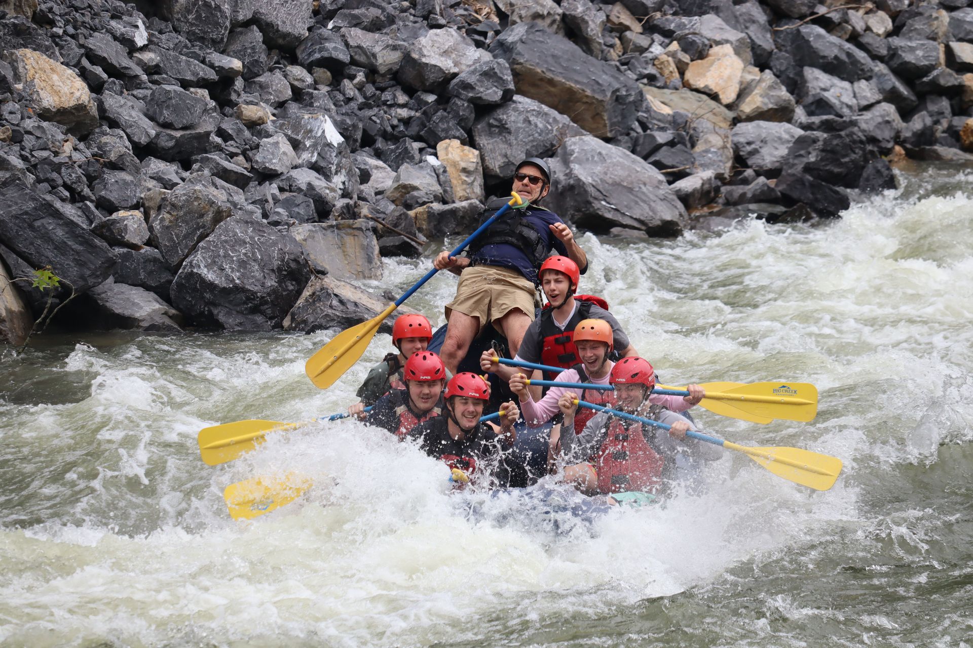 Whitewater rafters in red helmets paddling through rapids near rocky riverbanks