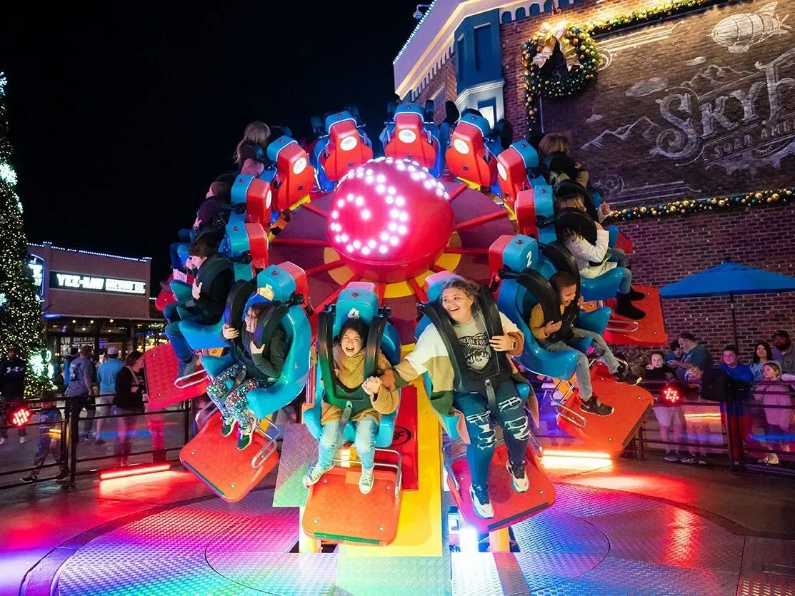 Thrill ride spinning at a carnival at night, with bright neon lights and riders leaning forward.