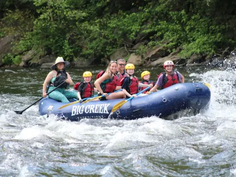 Six people whitewater rafting in a blue Big Creek raft on a rocky river