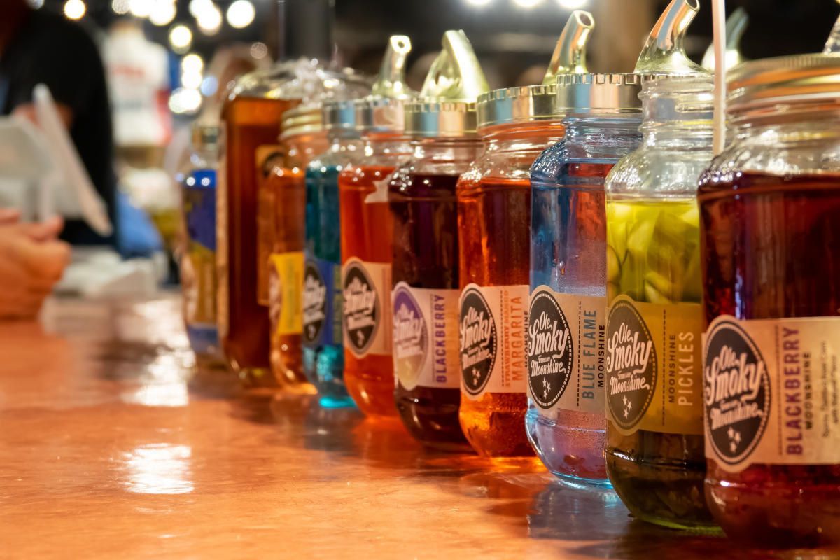 Colorful glass beverage bottles lined up on a wooden bar counter with a blurred background