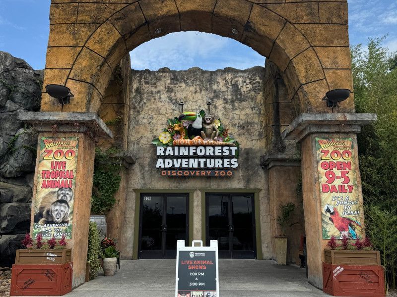 Entrance to Rainforest Adventures under a stone arch, with colorful signs and a ticket counter.