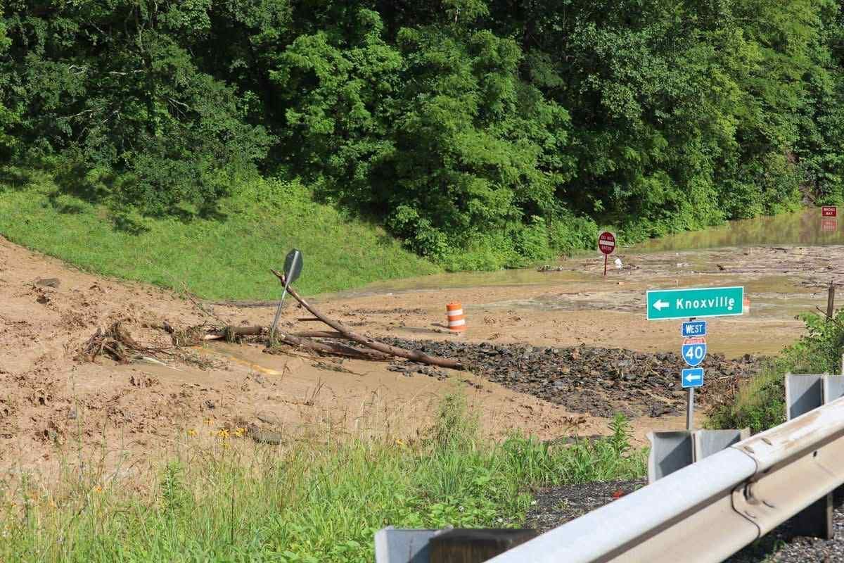 A muddy construction site or landslide area with a downed road sign and a green road sign pointing left.