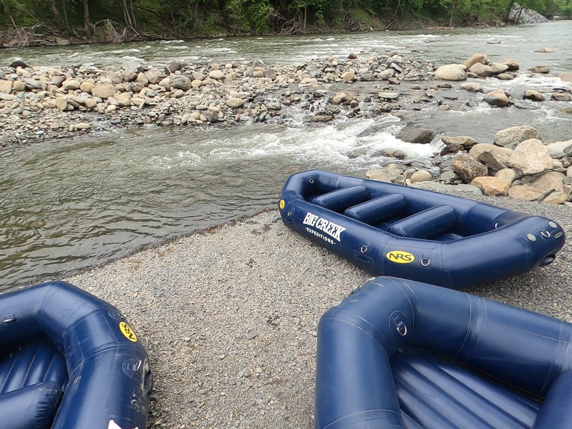 Blue inflatable rafts on a rocky riverbank beside rushing water and trees