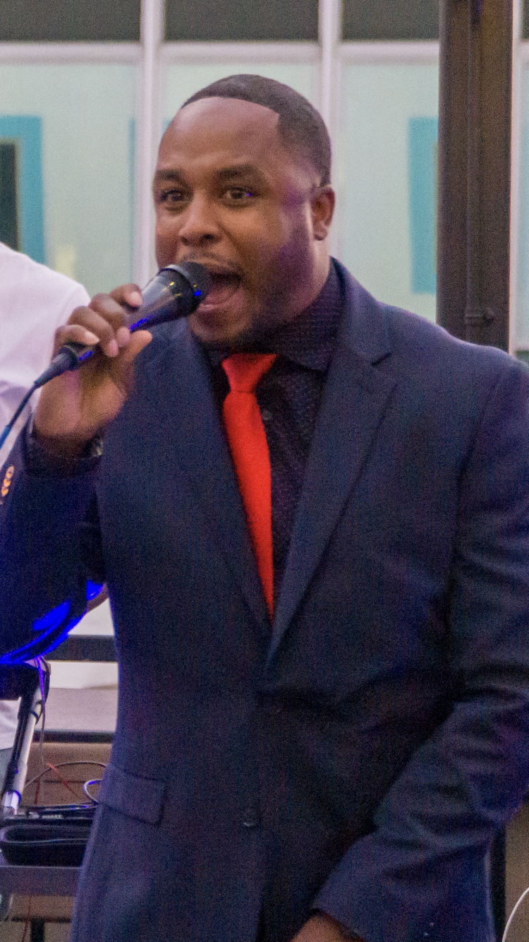 Chris in suit with red tie sings into microphone.