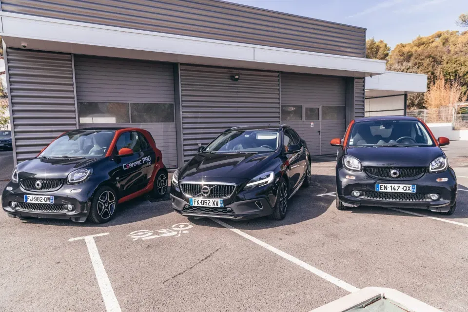 Trois voitures sont garées sur un parking devant un immeuble.