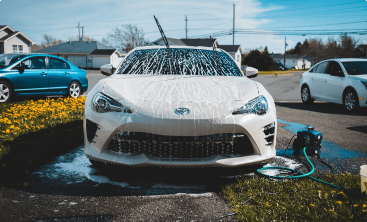 Une voiture blanche est lavée avec un tuyau dans un parking.
