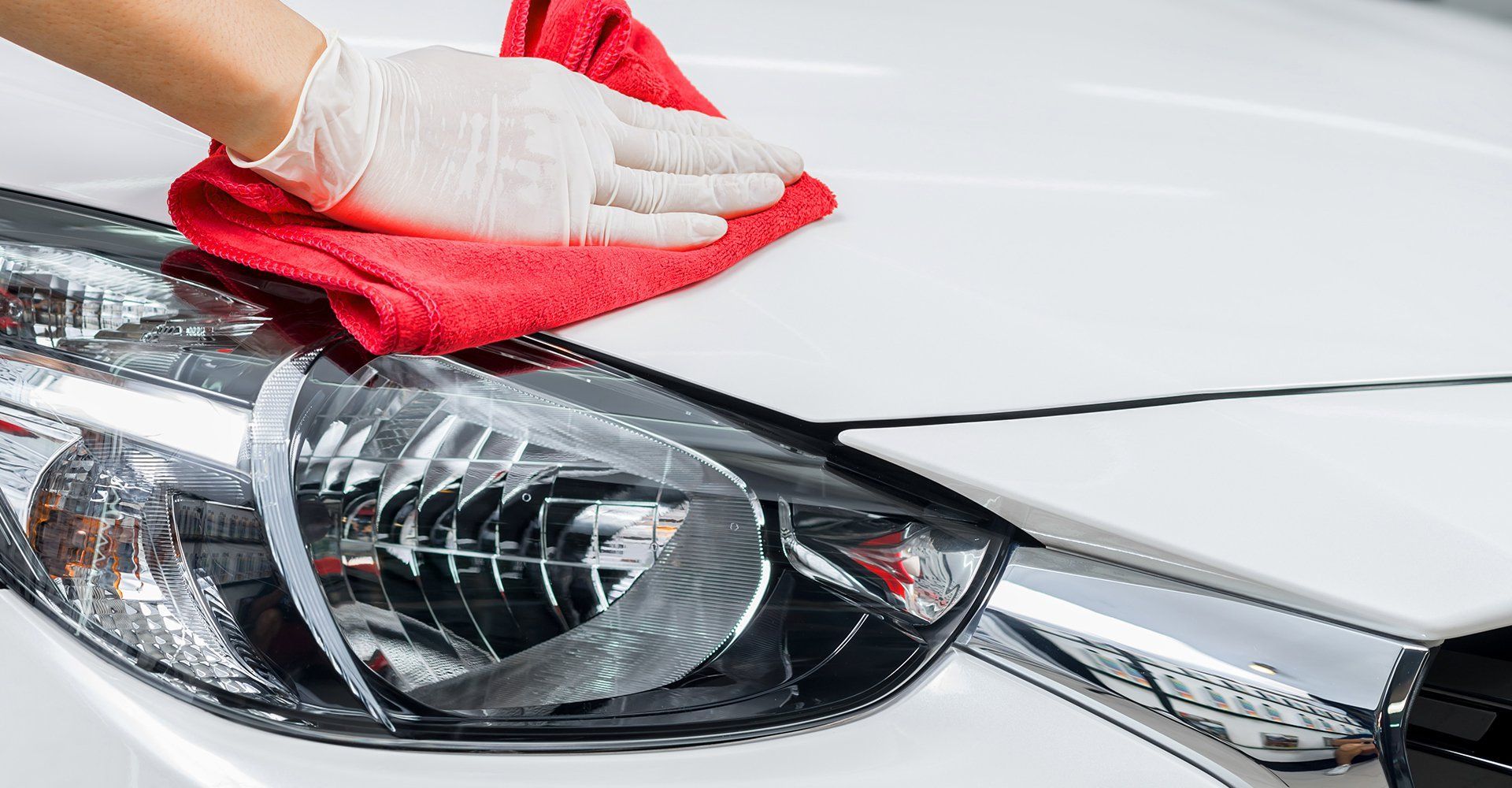 Une personne nettoie une voiture blanche avec une serviette rouge.