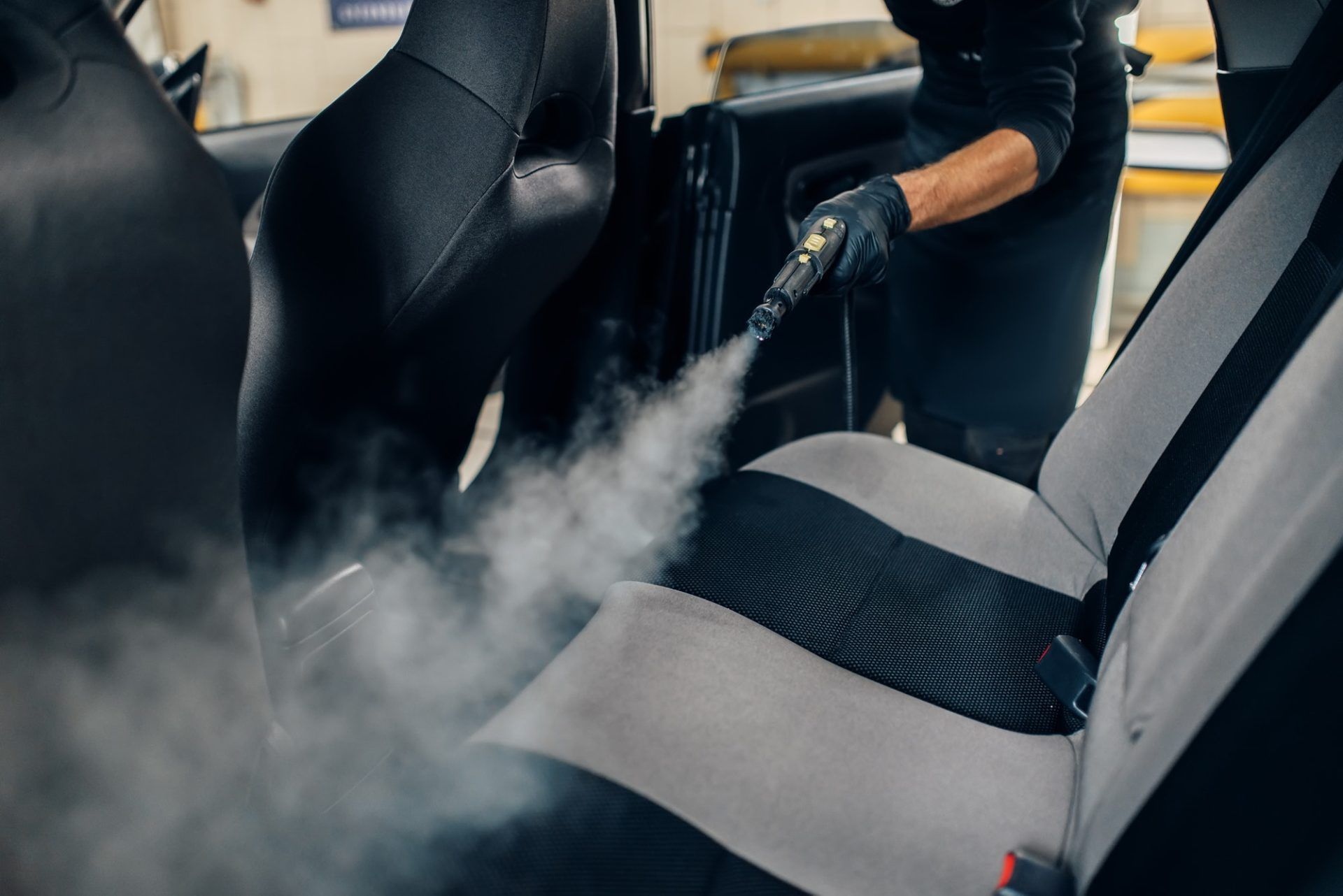 Une personne nettoie les sièges d'une voiture avec un nettoyeur à vapeur.
