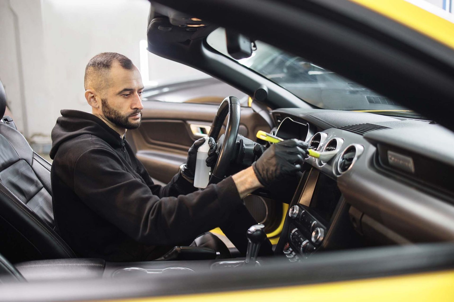 Un homme nettoie l'intérieur d'une voiture jaune.