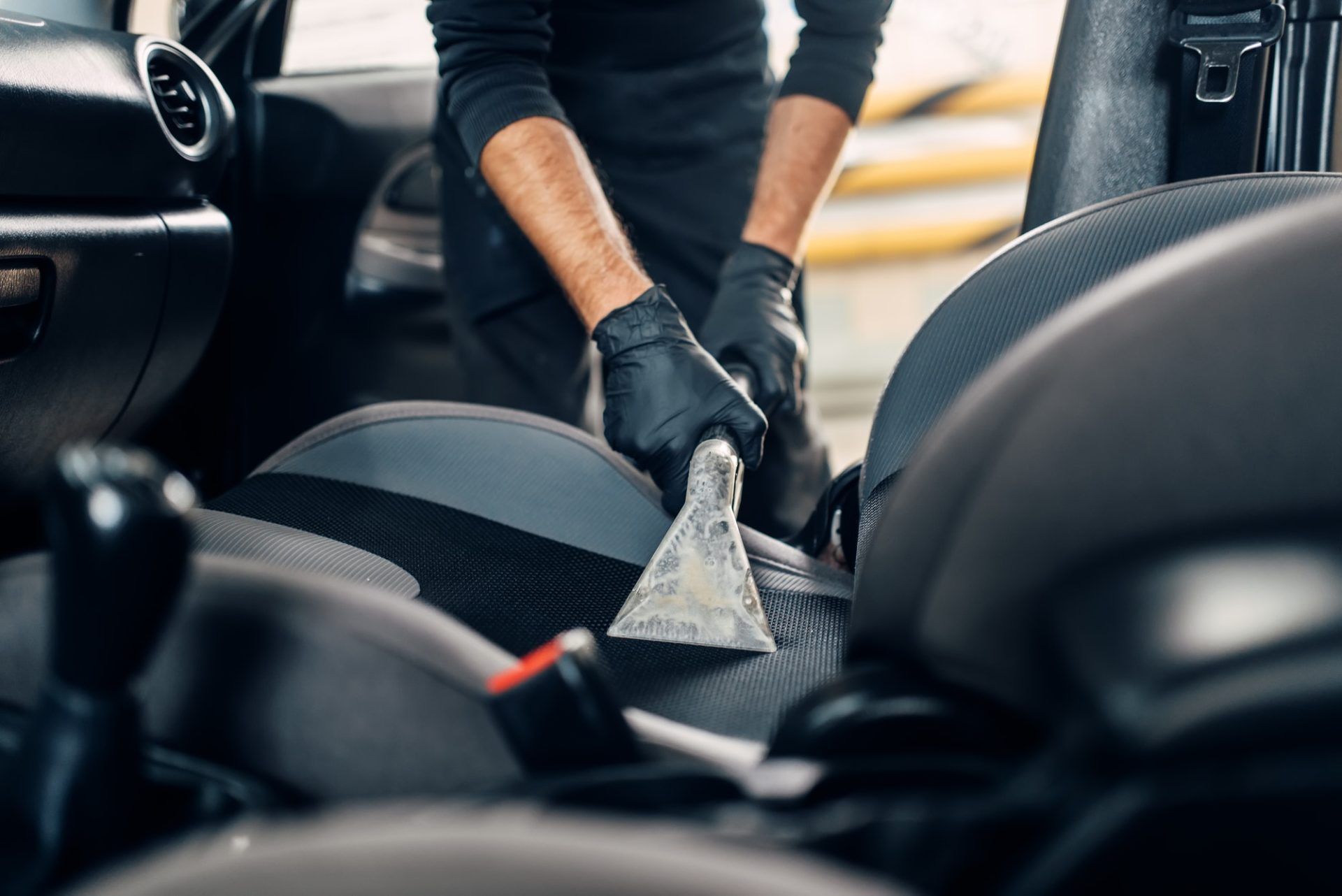 Un homme nettoie les sièges d'une voiture avec un aspirateur.