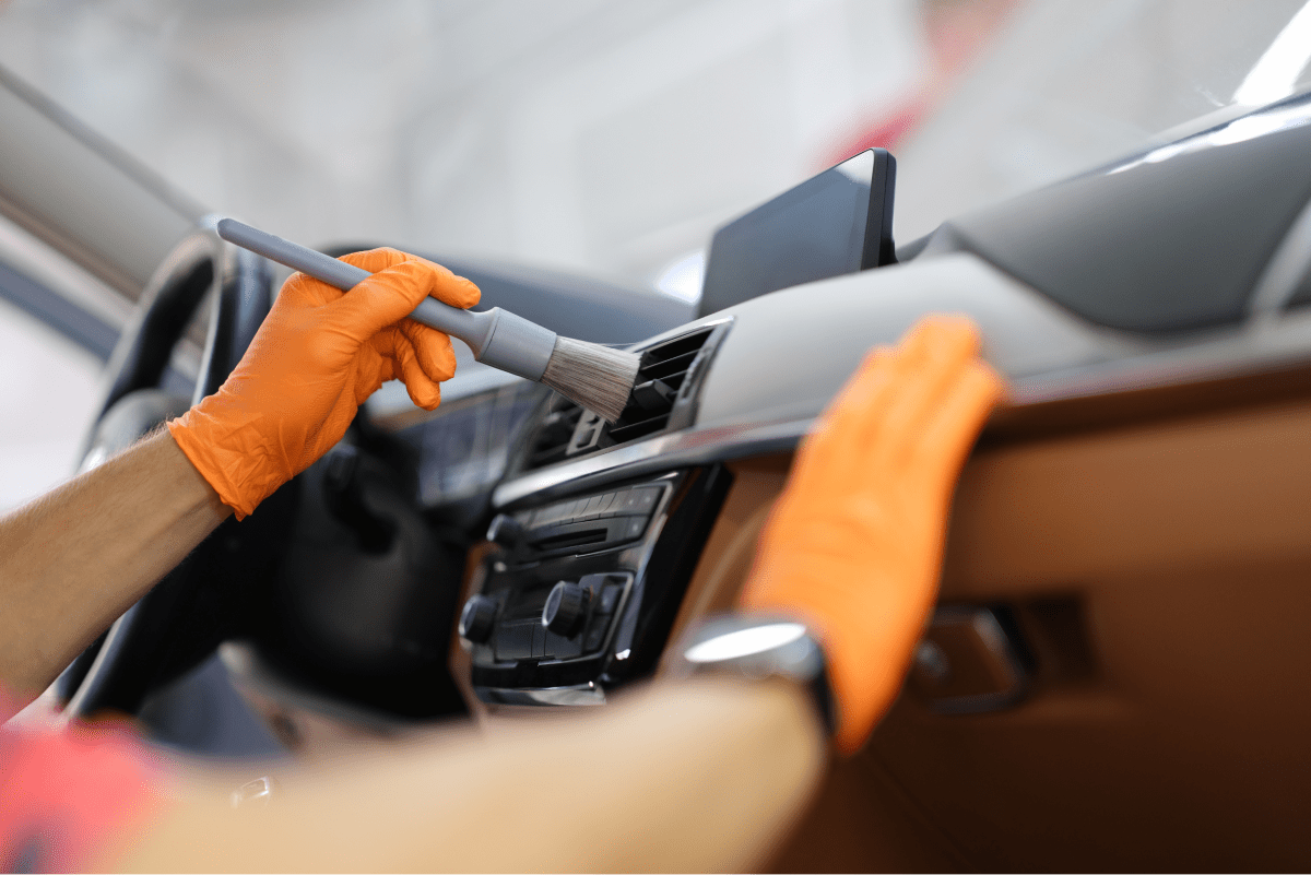 Une personne nettoie le tableau de bord d'une voiture avec une brosse.