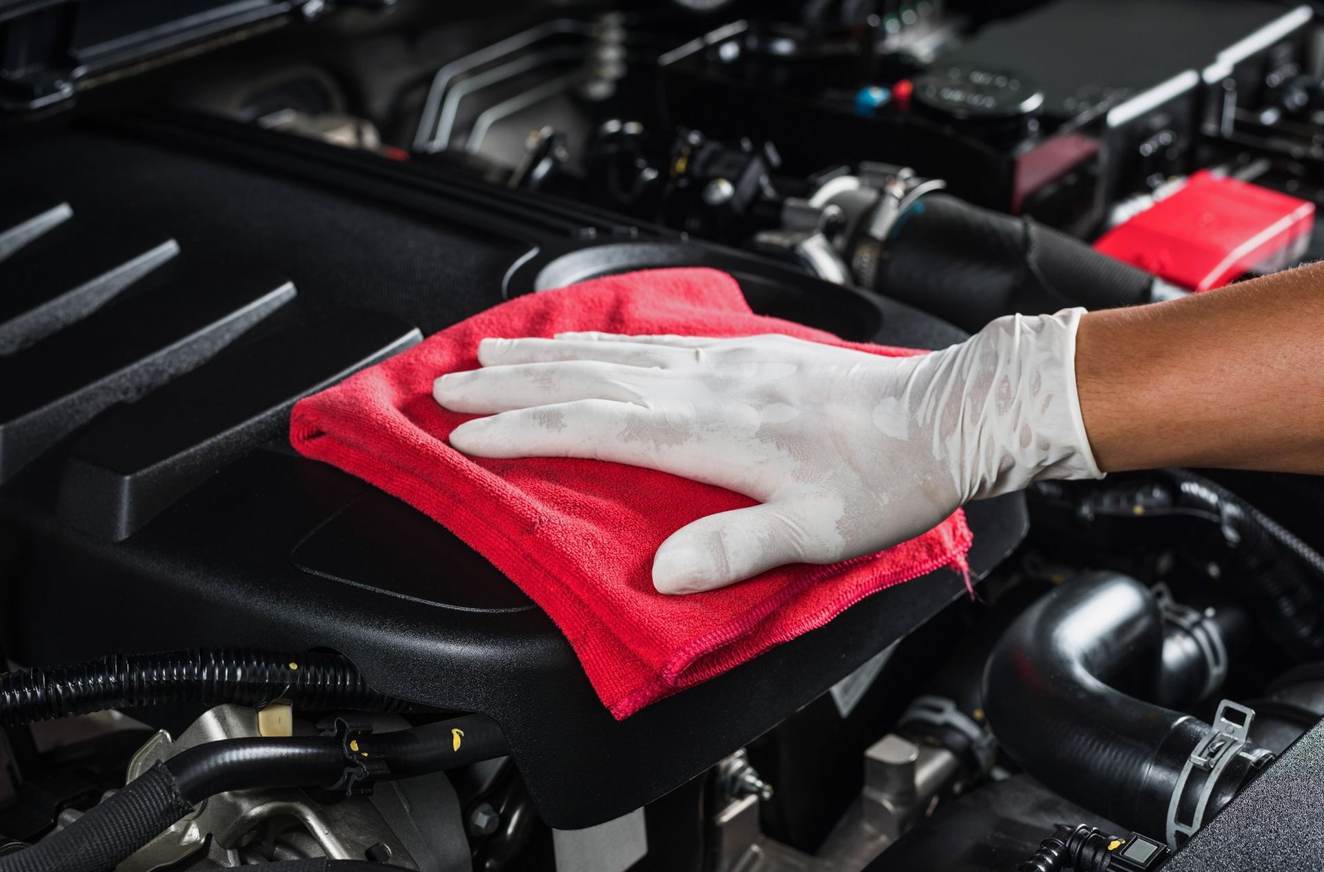Une personne nettoie le moteur d'une voiture avec une serviette rouge.