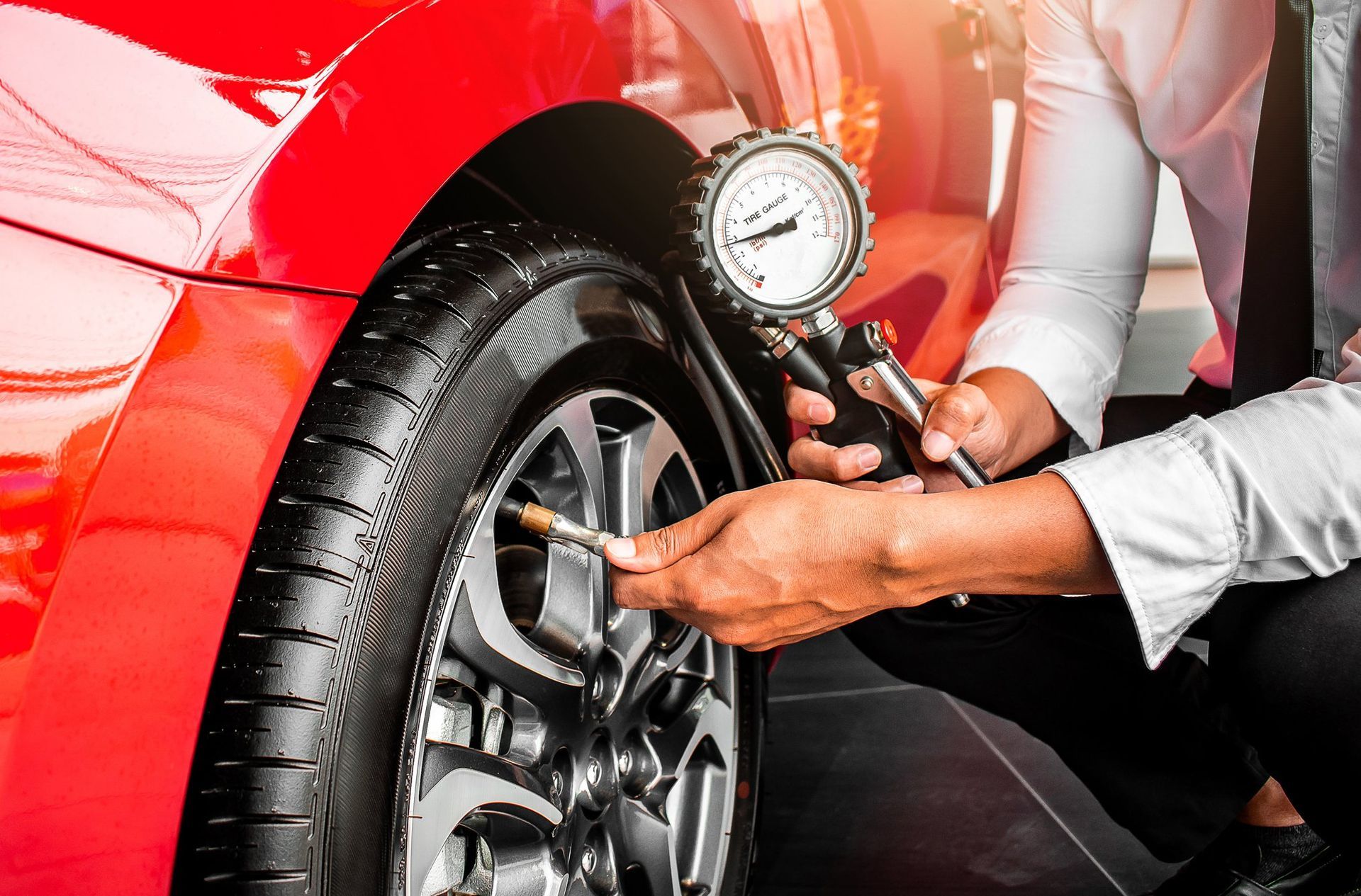 Un homme vérifie la pression des pneus d'une voiture rouge.